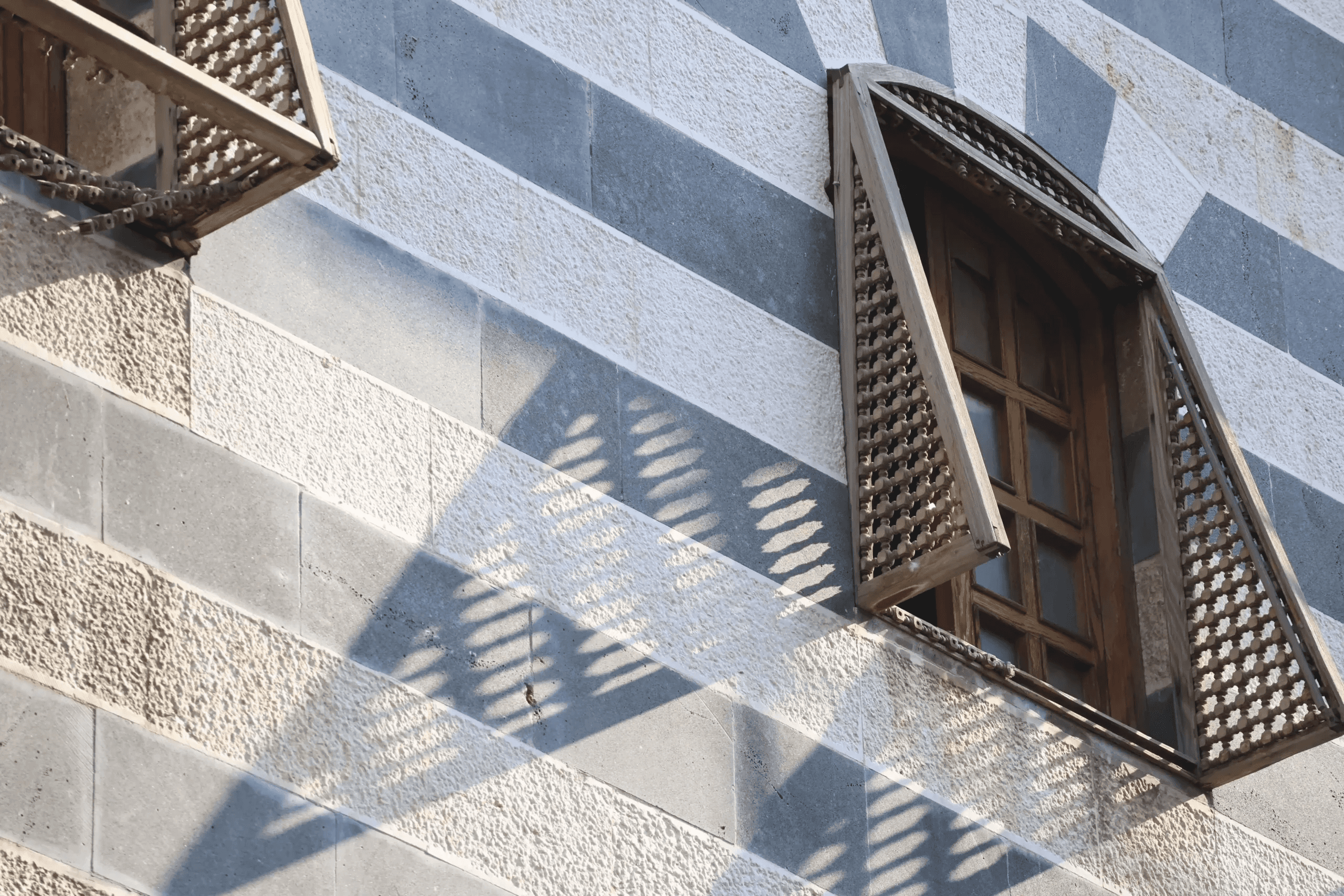 Turned wood mashrabiya screen casting shadows on a banded stone wall in Damascus